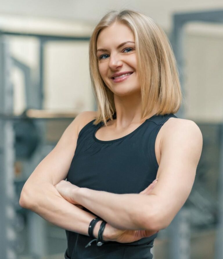 portrait-of-adult-blonde-fitness-woman-personal-trainer-with-folded-hands-in-gym-e1647224039242